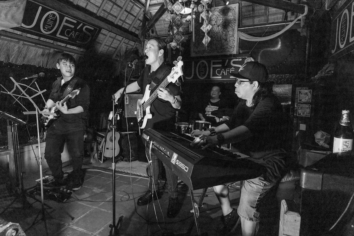 a band playing on a stage; there are two guitarists, a keyboardist and a drummer. this show is at a place owned by a small venue owner.