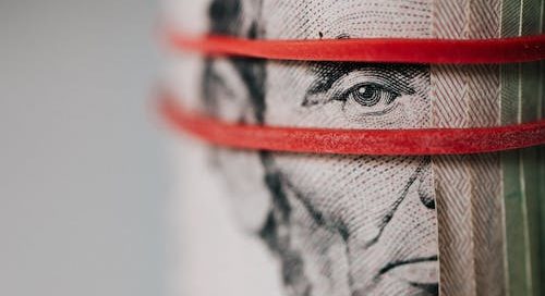 A stack of dollar bills is wrapped in a red rubber band. Abraham Lincoln, on the face of the $1 bill, is shown. payouts issues online have complicated cashflow for adult content creators.