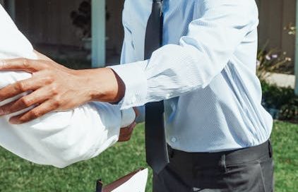 real estate agent standing next to a "For Sale" sign and shaking someone's hand; a "Sold" sticker is affixed to the sign