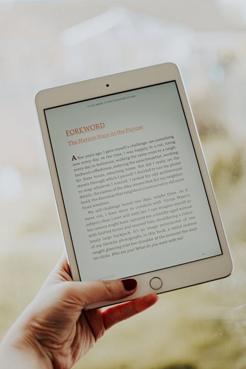 a person is holding an iPad in their hand. At least one of their nails is painted, and an e-book is open on the screen. E-book authors should be informed on the advantages of receiving their royalties via ACH versus other traditional methods of payment.